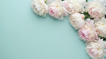 Soft pink peonies arranged on mint green background creating elegant floral border with copy space for wedding invitations and spring designs.