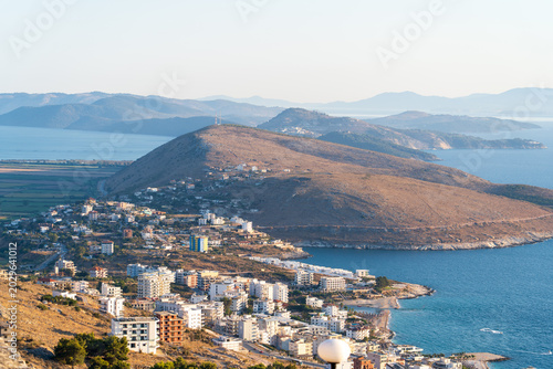 Saranda, Albania - August 24, 2025: High angle view of a suburban coastal area with hotels and residential buildings built on the slopes of a dry hill by the Ionian sea
