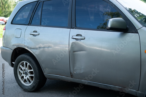 Obraz na plátně Close-up of a dented and scratched silver car door after a traffic accident, auto body damage concept