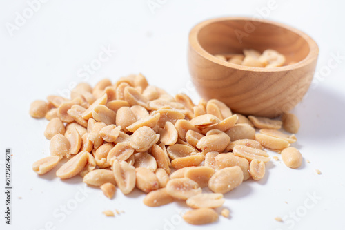 Peanuts in a wooden cup rest on a white background, creating a warm and rustic food-themed scene.