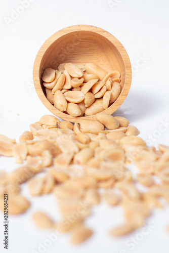 Peanuts in a wooden cup rest on a white background, creating a warm and rustic food-themed scene.