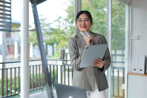 Young entrepreneur wearing glasses thinking and planning new business ideas while holding a digital tablet in modern office