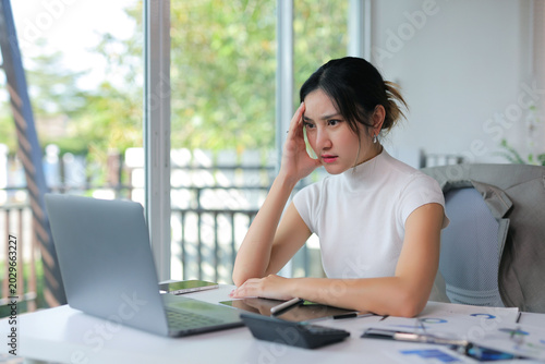 Young businesswoman suffering from headache and stress, overworking in a modern office or home, feeling overwhelmed and exhausted