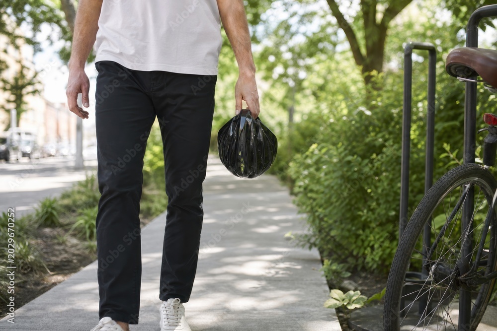 Fototapeta premium Casual urban individual carrying black compostable trash bag along green pedestrian pathway, eco-friendly waste disposal, sustainable lifestyle concept during daytime