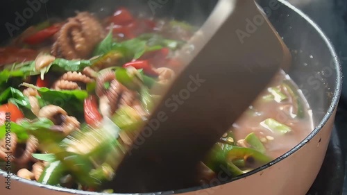 Close-up of spicy stir-fried baby octopus with red and green chili peppers cooking in a hot pan, authentic Asian seafood dish