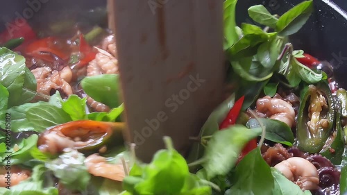 Close-up of spicy stir-fried baby octopus with red and green chili peppers cooking in a hot pan, authentic Asian seafood dish