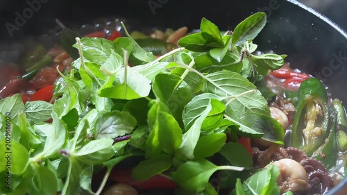 Close-up of spicy stir-fried baby octopus with red and green chili peppers cooking in a hot pan, authentic Asian seafood dish
