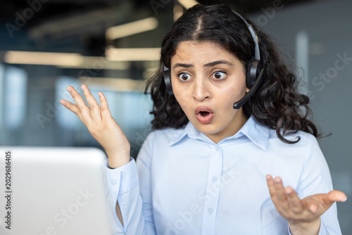 фотографія Young indian customer service agent in headset at laptop, wide-eyed and mouth op