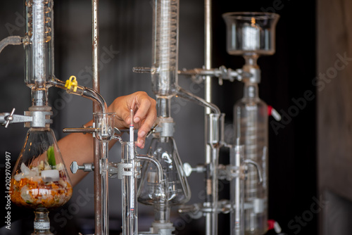 Canvas Print Close-up of a person adjusting a hydrometer inside a glass alcohol distillation apparatus in a laboratory setup