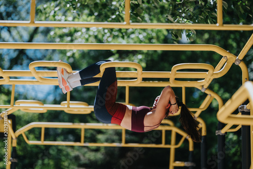 Canvas Print A fit woman performs a hanging leg raise on yellow outdoor monkey bars