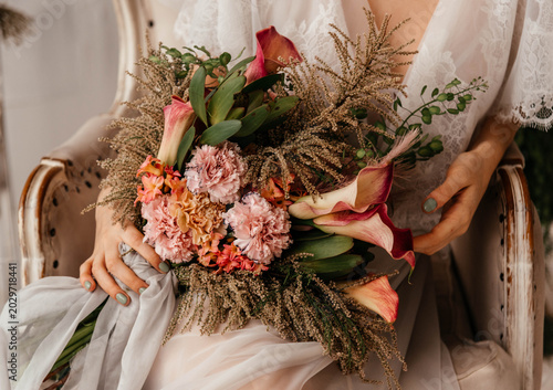 A girl holds a beautiful bouquet of flowers in her hands. Bridal bouquet. Carnations, calla lilies, dried flowers are collected in a composition. 