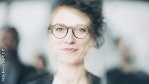 Smiling woman stands in front of group of people in blurred background during a business meeting in office