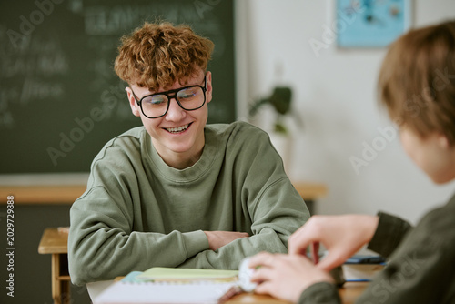 Foto Caucasian teenager boy smiling and studying with classmate in classroom, showing
