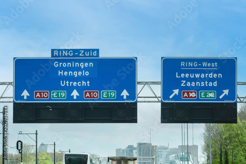 Daytime traffic on the A10 Amsterdam ring road with overhead signs for RING-Zuid and RING-West directing toward Groningen, Utrecht, Leeuwarden, and Zaanstad, Netherlands