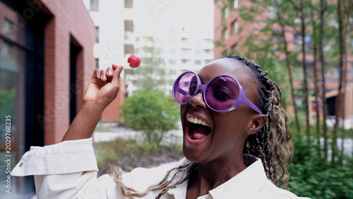 A beautiful woman poses for a smartphone selfie, holding a sweet lollipop.