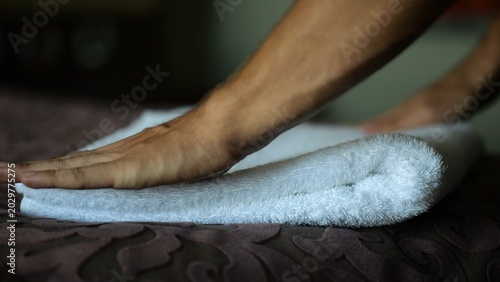 Fotografija Male hands of housekeeping adjusting soft white terry towel on a neatly made bed in a modern hotel room