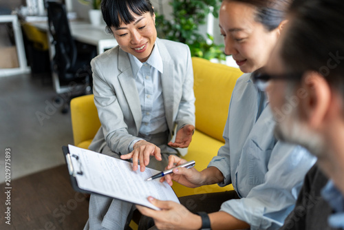Financial advisor handing contract for signature to multicultural clients during successful business meeting. Trust, agreement and professional consultation concept.