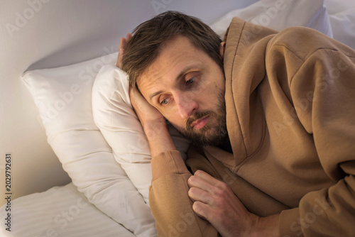 Foto Depressed exhausted man lying in bed with empty hopeless expression, wearing bro