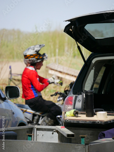 Motocross rider preparing for off-road race. Man in gear riding motorcycle near car. Extreme athlete getting ready to ride bike on circuit. Sports lifestyle and active hobby concept.