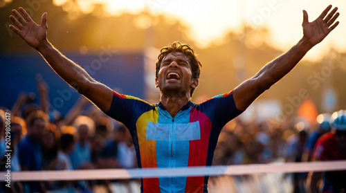 Cyclist triumphantly crossing finish line in grand tour sprint, arms raised in victory, colorful jersey, vibrant sunset background, cheering crowd