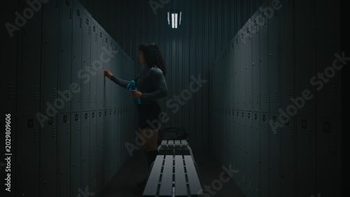 Tableau sur toile Focused Female Athlete Finishing Pre Training Ritual in Moody Gym Locker Room