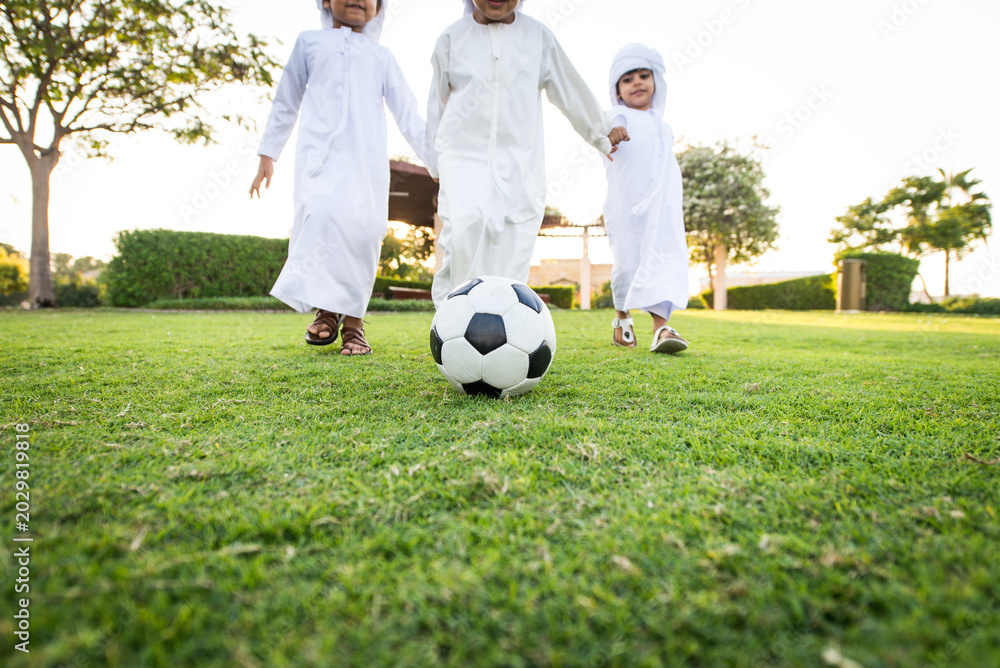 Obraz premium Arab kids wearing traditional emirati clothing meeting and having fun outdoors - Middle eastern boys bonding at the park in Dubai