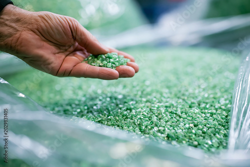 A close-up shot of a hand holding green polymer granulate pellets in a factory setting, showcasing raw materials like polypropylene, ASA, or PA for plastic manufacturing and industrial production.