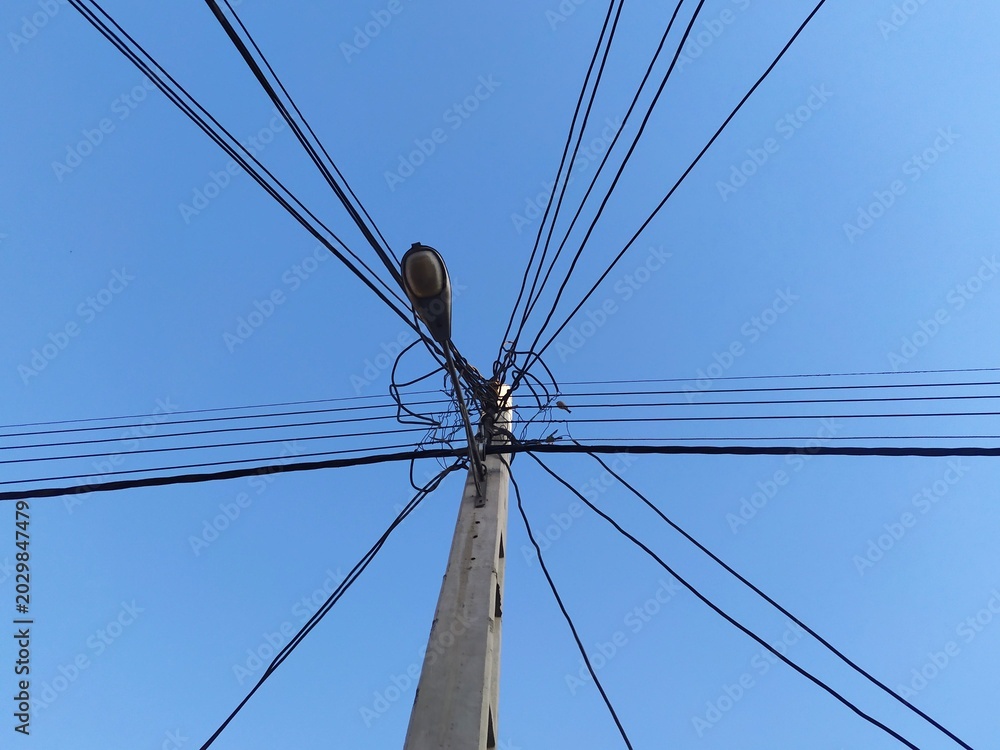 Fototapeta premium Tall utility pole with complex network of power lines against clear blue sky. Industrial infrastructure element creating strong geometric pattern and urban landscape feel.