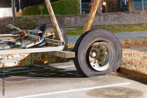 Quadro su tela Rusty trailer with flat tire parked on asphalt near grass and curb