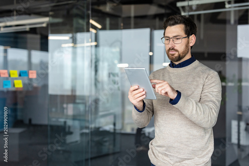 Cuadro en lienzo Professional man wearing glasses and a sweater standing in a contemporary office