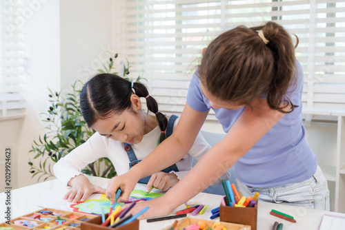 Foto Asian girl concentrating drawing paper with crayons while caucasian classmate as