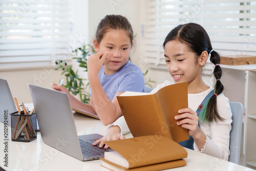 Billede på lærred Asian preteen girl smiling while holding notebook with caucasian classmate point