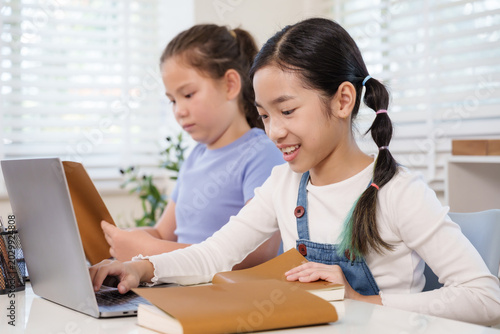 Картината върху платно Asian schoolgirl smiling working laptop computer beside caucasian classmate read