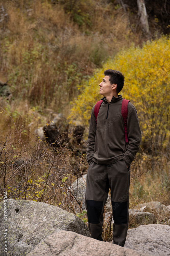 Fototapeta premium A young hiker stands on a rock, admiring the autumn scenery