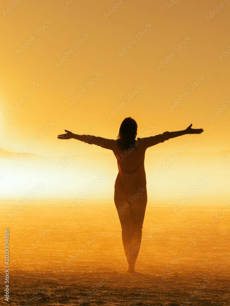 Fototapeta premium Silhouette of a mature female figure stands with arms open wide in a vast landscape under warm golden light, symbolizing a new chapter of life.