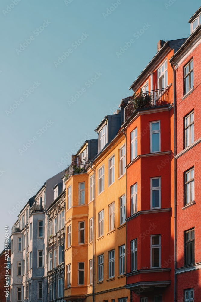 Fototapeta premium Vibrant, bright colors adorn the buildings lining a lively street, set against a clear blue sky in an urban area during the warm afternoon hours