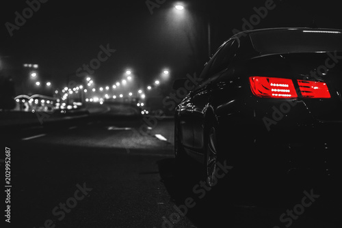 Quadro em tela Black car with red taillights on dark city street at night
