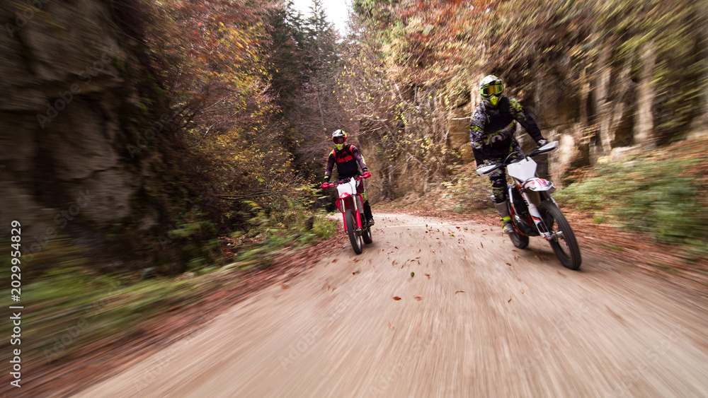 Fototapeta premium Motocross riders off-roading through autumn forest road