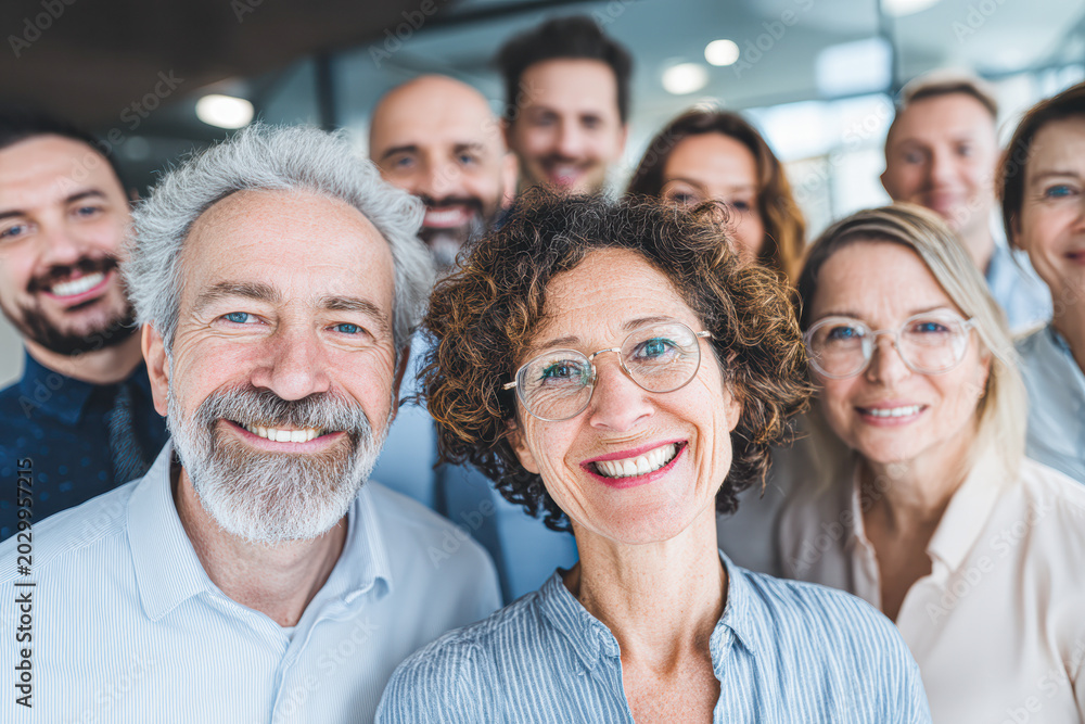 Fototapeta premium A group of smiling adults poses closely together, conveying happiness, teamwork, and a positive atmosphere in a modern indoor setting.