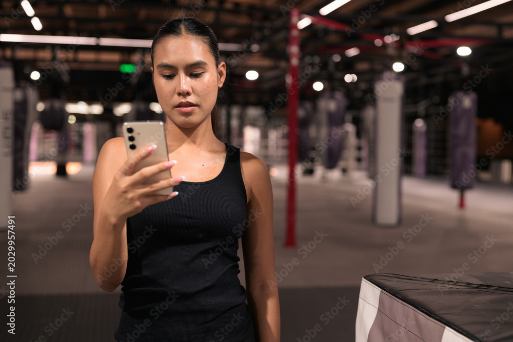 Fototapeta premium Female Athlete Using Smartphone Inside Boxing Gym