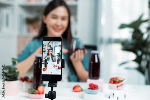Photography Selective focus smartphone with smiling young beautiful Asian reviewing mixed strawberry and cherry juice detox drink, presenting healthy product promotion selling on social media online