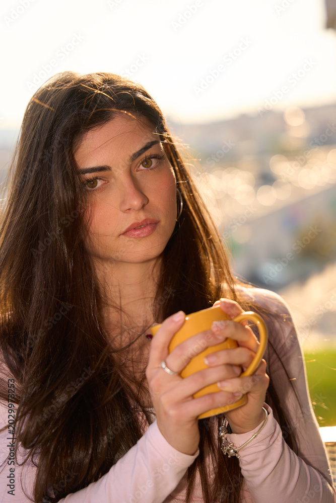Fototapeta premium Young woman enjoying coffee outdoors in sunlight