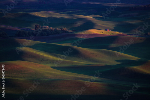 Landscapes of lushly green rolling hills with small red farm house in distance. lights and shadows make a dramatic scenery 