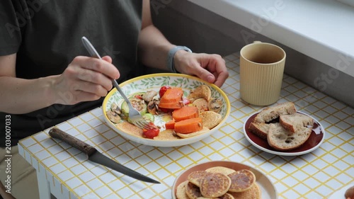 person eats breakfast or lunch in kitchen. delicious and healthy food cooked at home. woman eats sweet potatoes carrots with fork. drink coffee. vegetarian diet for body health. high quality 4k video