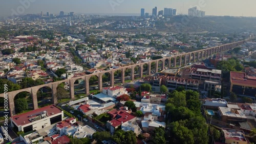 Traveling right aerial shot following Aqueduct of Queretaro with moving cars and residential district in Santiago de Queretaro Mexico showing historic urban infrastructure