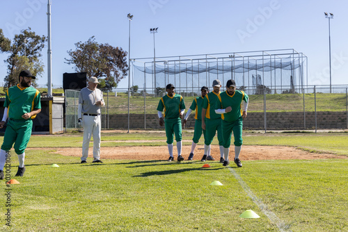 Fotografie Male players in green yellow uniforms practicing drills by infield with cones co