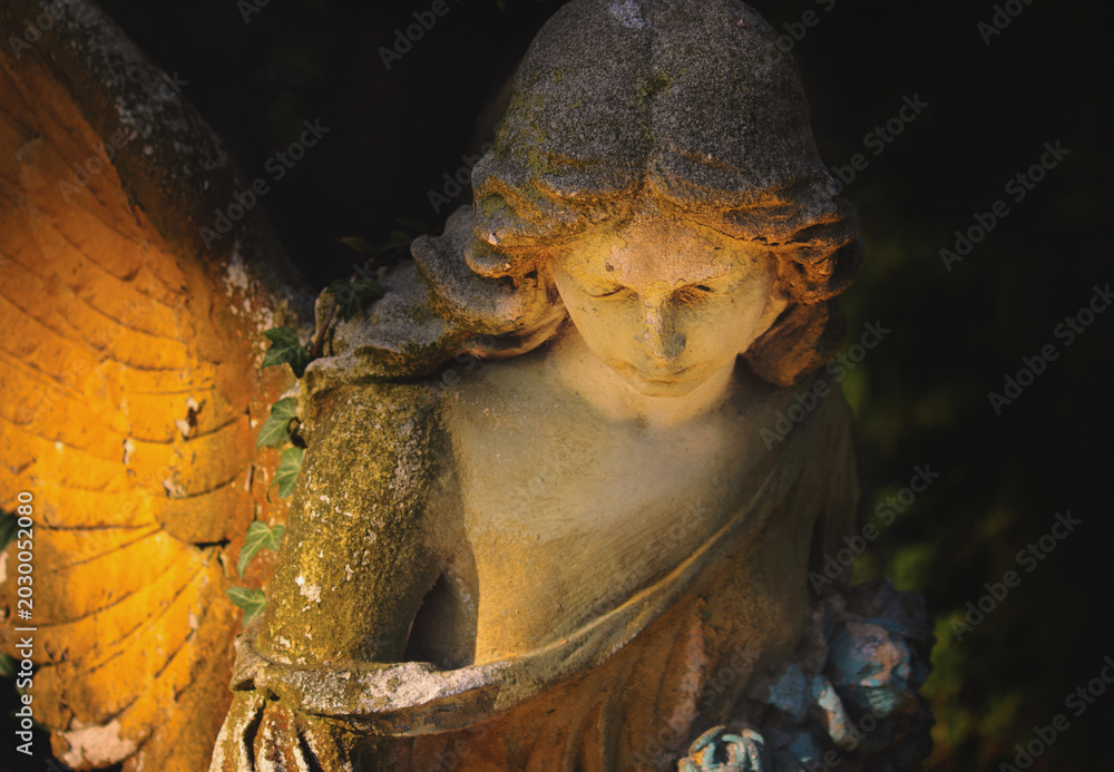 Fototapeta premium Glowing angel statue illuminated by warm golden light in darkness