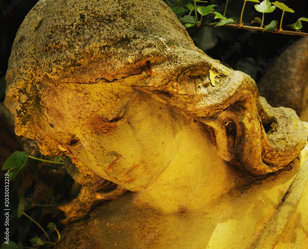 Fototapeta premium Golden light illuminating ancient angel statue in cemetery garden