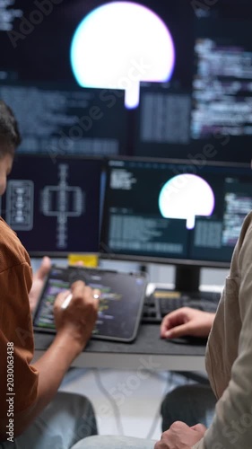 Over the shoulder view of tech developers analyzing software coding lines and circuit architectures across dual monitor desktop screens in a startup office.