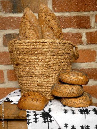 Foto A rustic woven basket overflows with baguettes, while a few round rolls and a square bun sit in front on a patterned cloth